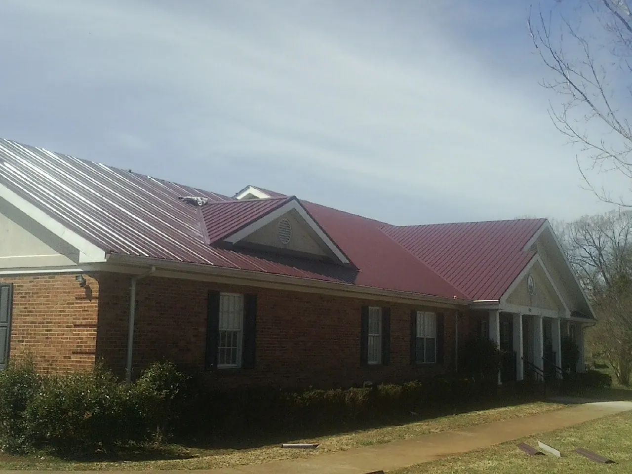 Red metal roof with gabled entries on a long brick building, from a Hail Damage Roof Repair job in Edinboro