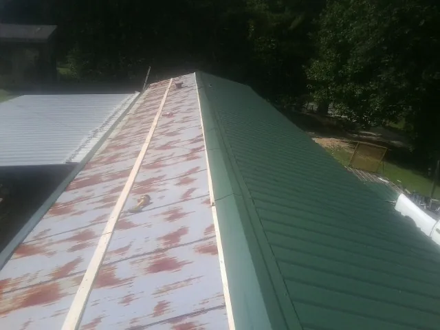 Old rusted panels beside newly installed green metal roofing — Wind Damage Roof Repair by Roofing Brothers in Edinboro