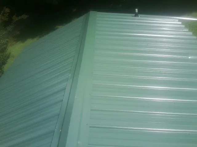 New green metal panels meeting at the ridge of a roof — Flat Roof Repair work by our crew in Edinboro