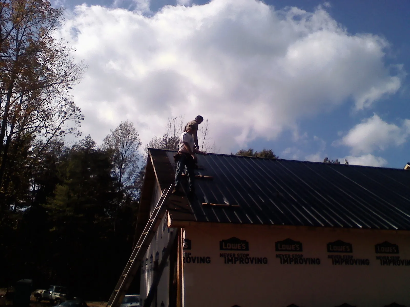 Roofer fastening dark metal panels high against a cloudy sky, from a Roof Inspection job in Edinboro