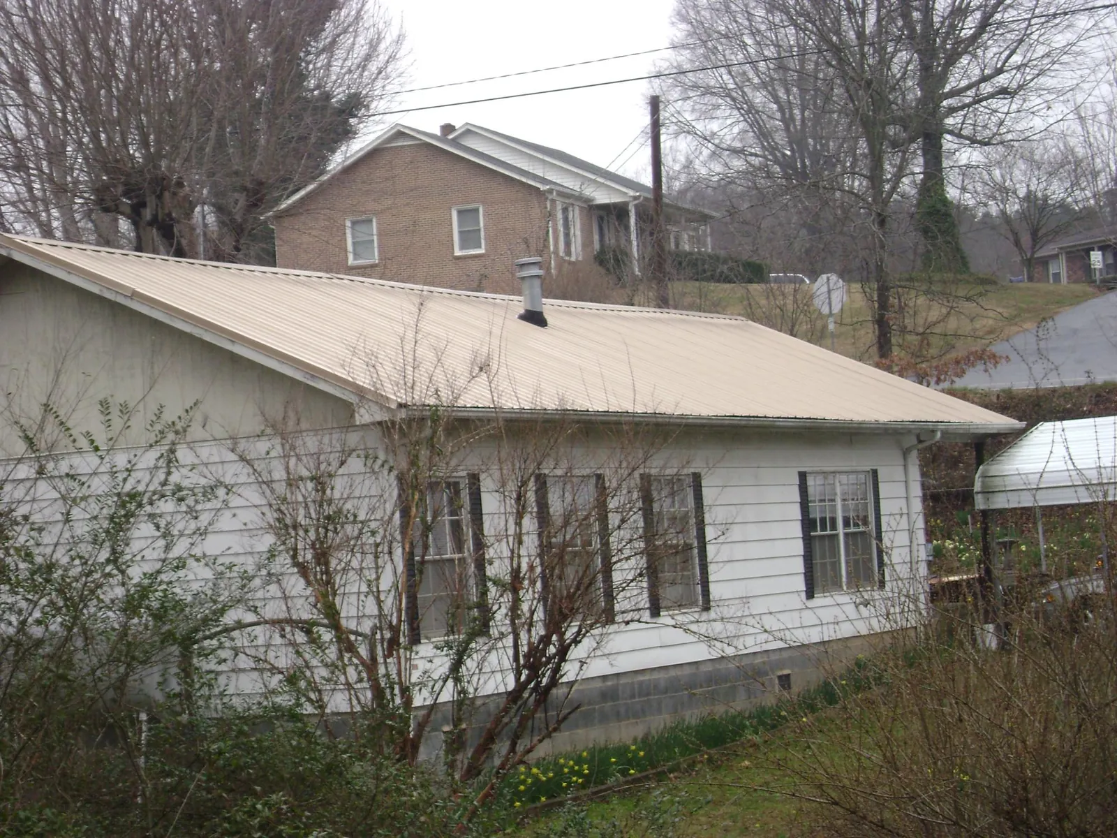 Tan metal roof on a white sided house set into a hillside — Commercial Roofing by Roofing Brothers in Edinboro