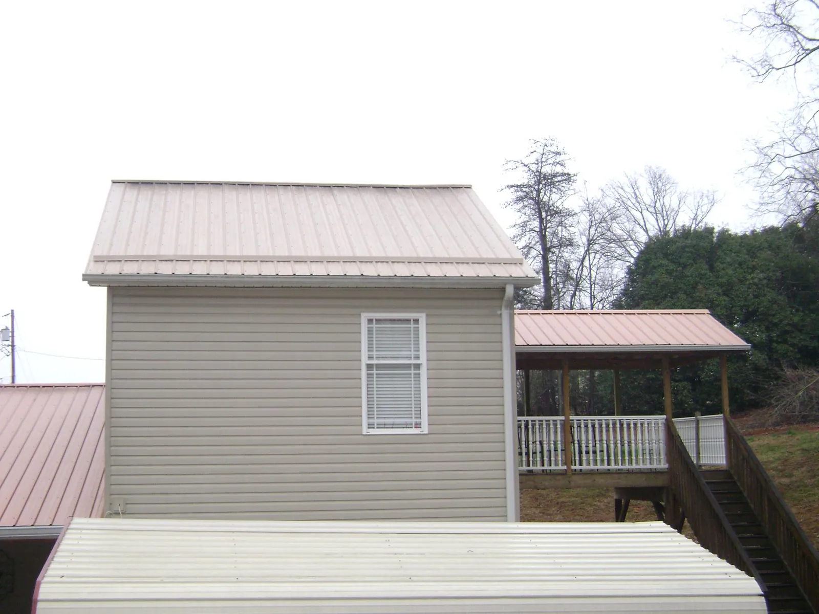 Tan metal roofs on a two story addition and attached porch, from a Roof Replacement job in Edinboro